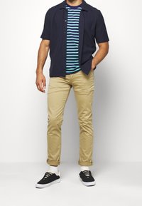 Short-sleeve navy button-up shirt over a striped teal and blue t-shirt; paired with khaki pants and black sneakers.