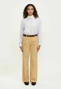 Lichtpaars shirt met lange mouwen en knopen, gecombineerd met beige hoge taille wijde broek, accentueert door een bruine riem en donkere schoenen.