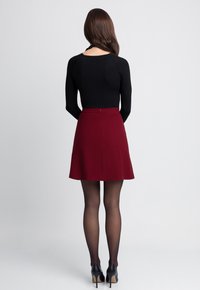 Czarna bluzka z długim rękawem w zestawieniu z bordową spódnicą w kształcie dzwonu. Modelka nosi przezroczyste czarne rajstopy oraz czarne szpilki.