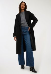 Długi czarny płaszcz na szarym swetrze, zestawiony z szerokimi niebieskimi dżinsami i czarnymi botkami na obcasie. Gładki materiał ze wyraźną konstrukcją.