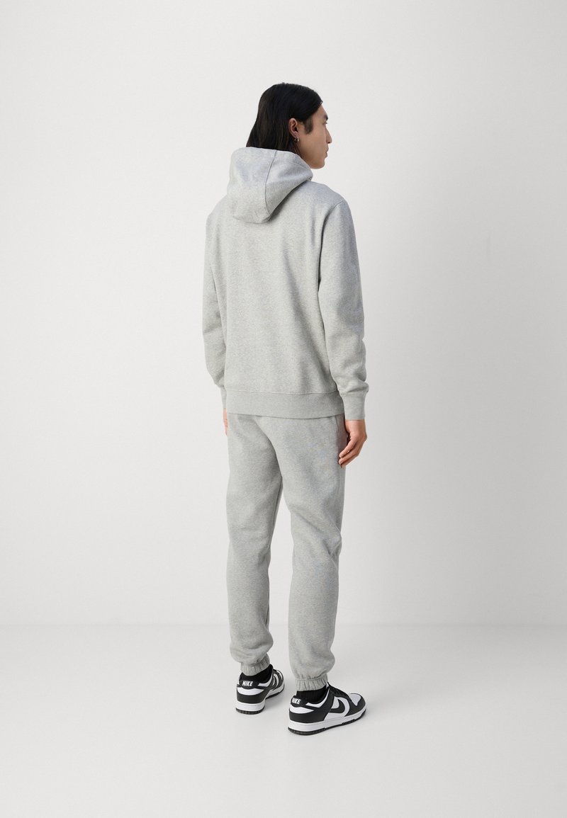 Graues Baumwoll-Hoodie- und Jogginganzug-Set, ausgestattet mit einer Kordelzugkapuze, gerippten Bündchen und Seitentaschen, kombiniert mit schwarzen Sportschuhen.