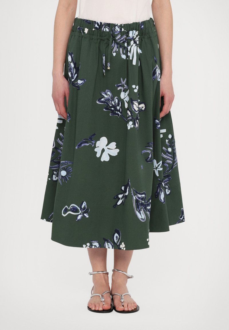 Fustă florală verde cu talie elastică plisată, având modele albastre și albe. Până la genunchi, asociată cu sandale argintii.