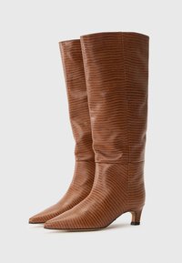 Bottes marron jusqu'au genou avec un motif texturé, bouts pointus et un petit talon carré. Fabriquées en matériau lisse avec une finition brillante.