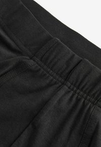 Schwarzer elastischer Bund mit geraffter Textur, kombiniert mit einem dunklen Stoff, der eine glatte Oberfläche zeigt. Einfaches, minimalistisches Design.