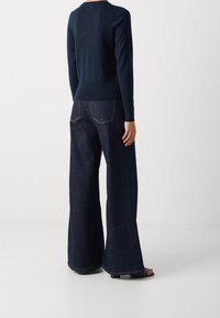 Námořnický svetr s přiléhavým pasem, zkombinovaný s širokými tmavými jeansy s viditelnými zadními kapsami a kontrastním šitím.