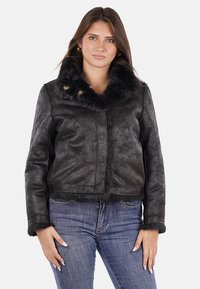Giubbotto in pelle sintetica nera con un colletto di pelliccia, design cropped, due bottoni dorati e dettagli in superficie testurizzati, abbinato a jeans di denim.