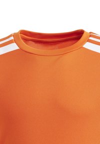 Oranžové atletické tričko s kulatým výstřihem, zdobené bílými horizontálními pruhy na ramenou a hladkým, strukturovaným materiálem.