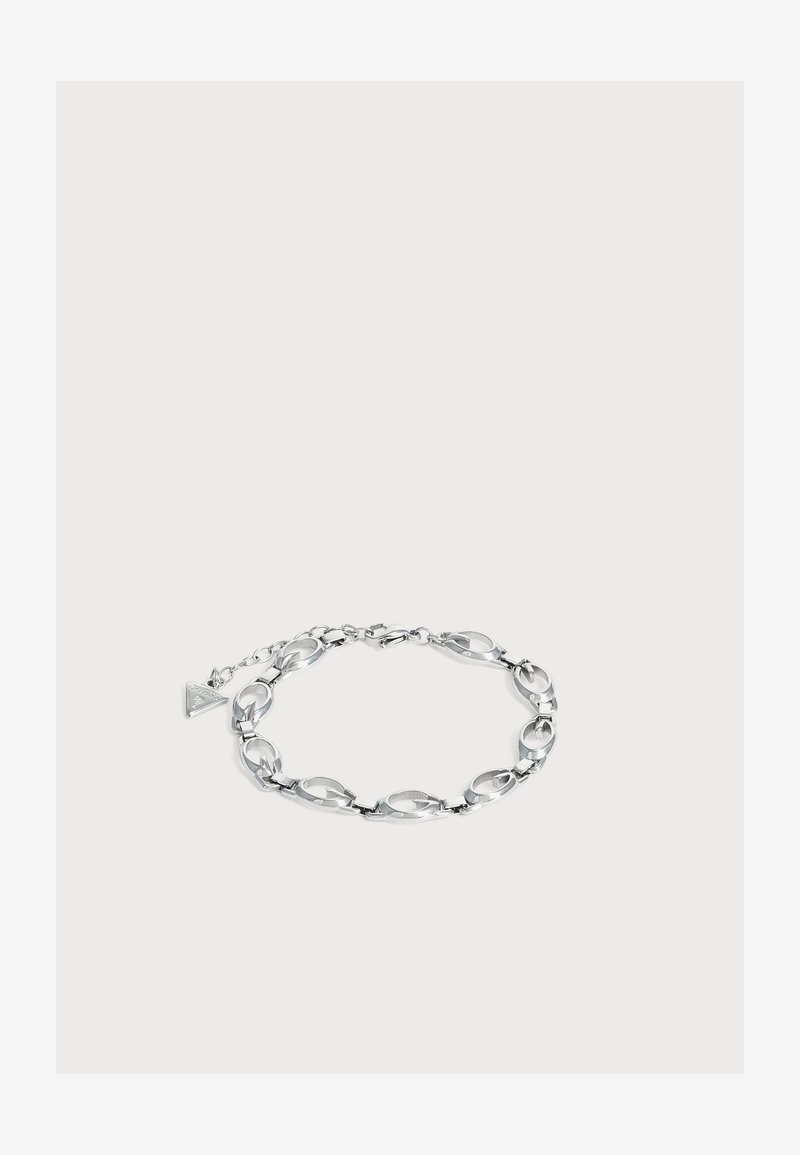 Bracelet chaîne en argent avec des maillons ovales et un petit charm triangulaire attaché près du fermoir homard sur un fond clair.