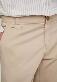 Pantalones de algodón beige con diseño de pierna recta, apertura de bolsillo frontal y cierre de botón. Textura suave con sutiles detalles de costura.