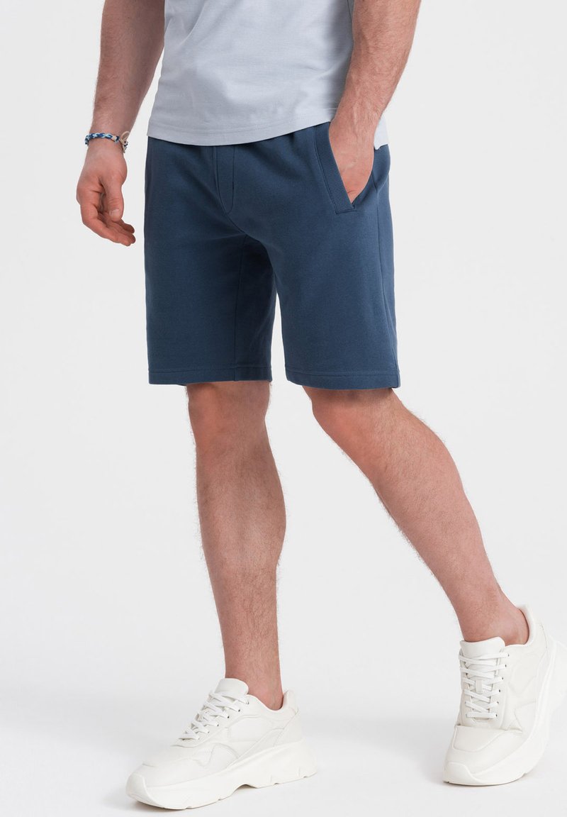 Shorts en coton bleu avec poches latérales, taille côtelée et coupe droite. Assortis avec des baskets blanches chunky. Design minimaliste.