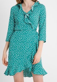 Tyrkysové šaty s tříčtvrtečn�ími rukávy, bílými puntíky, volánkovým výstřihem a rozšířeným spodním lemem. Vyrobené z lehkého materiálu.