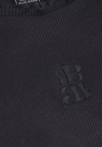 Svart ribbat tyg med en präglad logotyp till vänster. Texturen är mjuk och elastisk, vilket gör den lämplig för avslappnad klädsel.