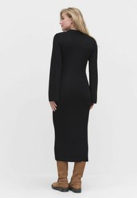 Mustat ribbed-kudotut mekko, jossa on pitkät hihat, tiukka siluetti ja midi-pituus. Yhdistettynä vaaleanruskeisiin polven korkuisiin saappaisiin, jotka näyttävät sileiltä.