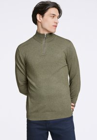 Sudadera de cuello con cremallera en verde oliva, fabricada en tejido de punto texturizado, con mangas largas y silueta ajustada, y con puños y dobladillo acanalados.