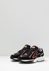 Svarta sneakers med orange accenter, suède och mesh material, rund tå, snörningsdesign, svart gummisula, och logotyp på tungan.