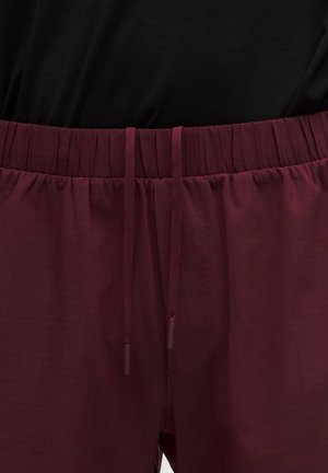 Közelkép a bordó rugalmas derékpántos nadrágról, elöl zsinórral, fekete felsővel viselve.