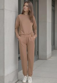 Beige sportief set bestaande uit een langemouwen top met ribbels aan de mouwen en bijpassende joggers met elastische rand, gecombineerd met witte sneakers.