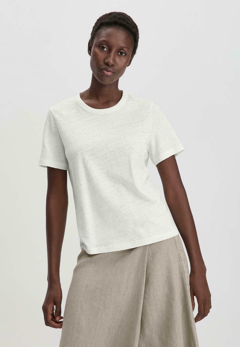 T-shirt blanc à manches courtes avec un col rond, fabriqué en tissu texturé, associé à une jupe en lin beige clair, design minimaliste.