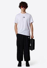 White short-sleeve t-shirt with black logo, black cargo pants with pockets, and black backpack. Large red sunglasses complete the look.