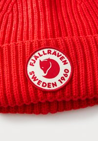 Červená rebrovaná pletená čiapka s okrúhlym bielym nášivkom s logom červeného líška a textom "Fjällräven Švédsko 1960."