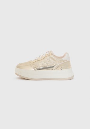 Zapatillas metálicas doradas con una parte superior texturizada, detalles en crema, cordones blancos y una suela blanca gruesa. Diseñadas con un acabado estampado.