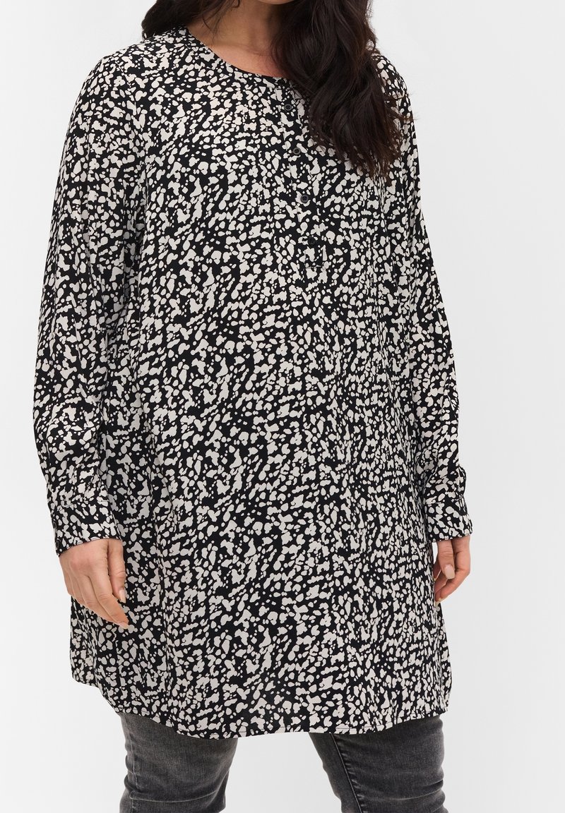 Tunique à motifs noirs et blancs, avec des manches longues, un col arrondi et une coupe ample, arborant un design abstrait éclaboussé.