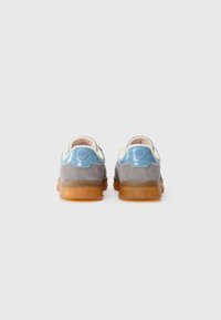 Un paio di sneaker in camoscio grigio con linguette blu sul tallone, interno bianco e suole in gomma traslucida marrone, viste da dietro su sfondo bianco.