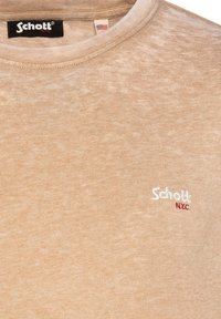 T-shirt beige a maniche corte realizzato in tessuto morbido, con scollo rotondo e logo ricamato "Schott NYC" in bianco e rosso.