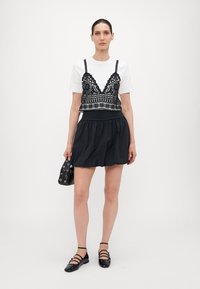Svart blonde crop-top over en hvit t-skjorte, paret med et svart elastisk midjebånd skjørt. Svart tilbehørsveske og svarte sandaletter med stropper.