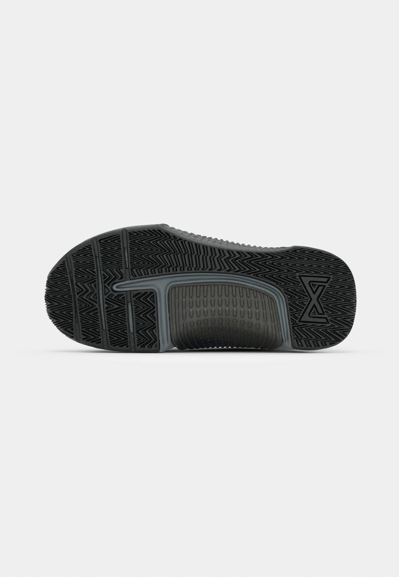 Semelle de chaussure de sport noire avec un motif texturé, présentant des rainures et des crêtes pour une meilleure adhérence, accentuée par une section centrale lisse et un détail de logo.