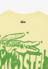 T-shirt en coton jaune avec un imprimé graphique de crocodile vert. Comprend un petit logo à l'arrière près du cou. Texture douce, design à manches courtes.