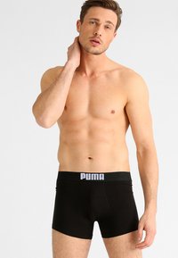 Zwarte boxershorts van rekbare stof, met een brede tailleband met witte "PUMA" branding. Het ontwerp is nauwsluitend met een gladde textuur.