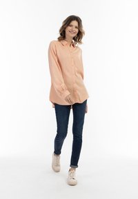 Ferskenfarvet, langærmet skjorte med krave og manchetter, parret med mørke skinny jeans og lyse sneakers.