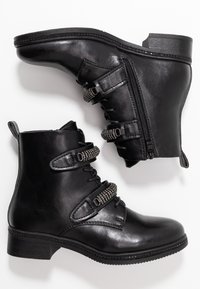 Botas de tobillo de cuero negro con punta redonda, correas texturizadas con acentos de hardware, cremallera lateral y un tacón bajo cuadrado.