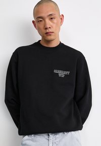 Black sweatshirt with long sleeves, round neckline, and "Carhartt WIP" embroidered logo on the left chest. Simple, minimalist design.