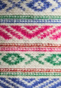Strickstoff mit geometrischen Mustern in Blau, Pink, Grün und Rot auf einem weißen Hintergrund, mit einer weichen, strukturierten Oberfläche.