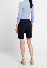 Pantalones cortos azul marino con corte relajado, cintura elástica y puños doblados. Combinados con una camiseta azul claro y sandalias de cuña beige.
