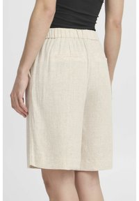 Shorts in lino beige con fascia elastica in vita e due tasche sul retro, presentati in un tessuto liscio e strutturato, mostrati di spalle.