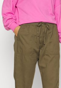 Khaki nedtrækspants med elastisk talje og snor, der har to forlommer og en afslappet pasform.