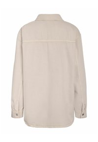 Bézs színű, hosszú ujjú ing gallérral és gombos mandzsettával. Egyetlen hátvarrással és az első vállrészlet díszítéssel rendelkezik. Organikus pamut anyagból készült.