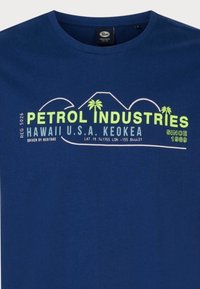 Námořnická modrá tričko vyrobené z bavlny; obsahuje potištěný grafický motiv s nápisem "PETROL INDUSTRIES", palmami a zeměpisnými souřadnicemi v zelené a bílé barvě.