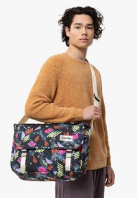 Borsa messenger nera con motivo astratto colorato, dotata di spallacci beige e chiusura a pattina. Il materiale appare sintetico e resistente.