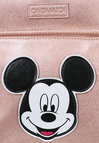 Zaino rosa oro con una texture metallica liscia, caratterizzato da una grande toppa nera e bianca di Topolino sulla tasca anteriore.