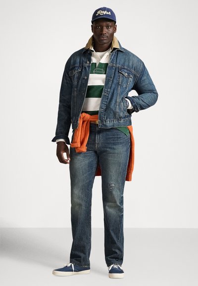 Muž nosiaci modrú rifľovú bundu a džínsy, zeleno-bielo pruhované tričko, oranžový sveter previazaný okolo pása, modrú čiapku a modré tenisky.