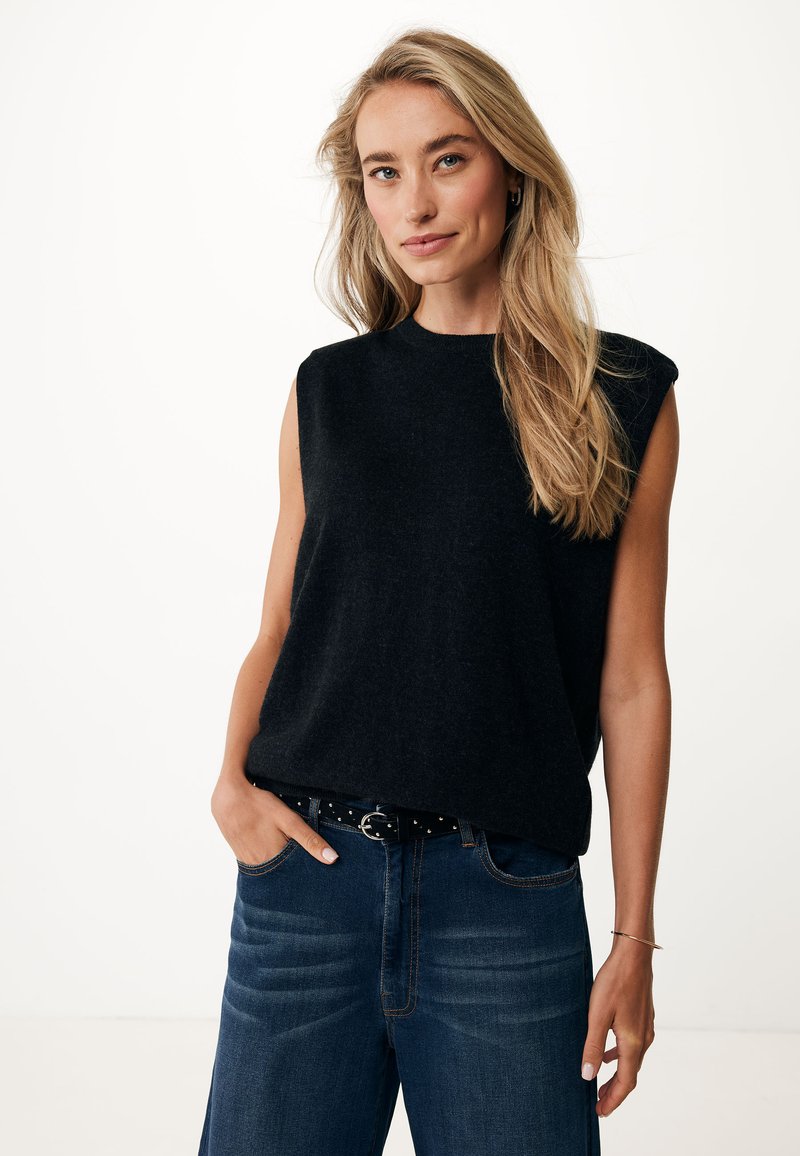 Top de punto sin mangas negro con cuello redondo, combinado con jeans de mezclilla oscuros y un cinturón negro con tachuelas; textura suave y corte relajado.