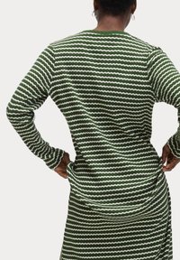 Grünes gestreiftes Langarmoberteil mit weißen gewellten Linien. Strukturierte Ripp-Textur, runder Halsausschnitt und enganliegende Ärmel. Natürlicher Stoffabschluss.