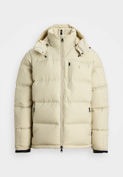 Light beige puffer jacket with a high collar, detachable hood, zippered front, and two side pockets. Features stitched panels and logo detail.