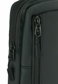 Zbliżenie rogu czarnej torby z teksturowanej tkaniny z widocznymi dwoma suwakami i uchwytami do oddzielnych przegrody.