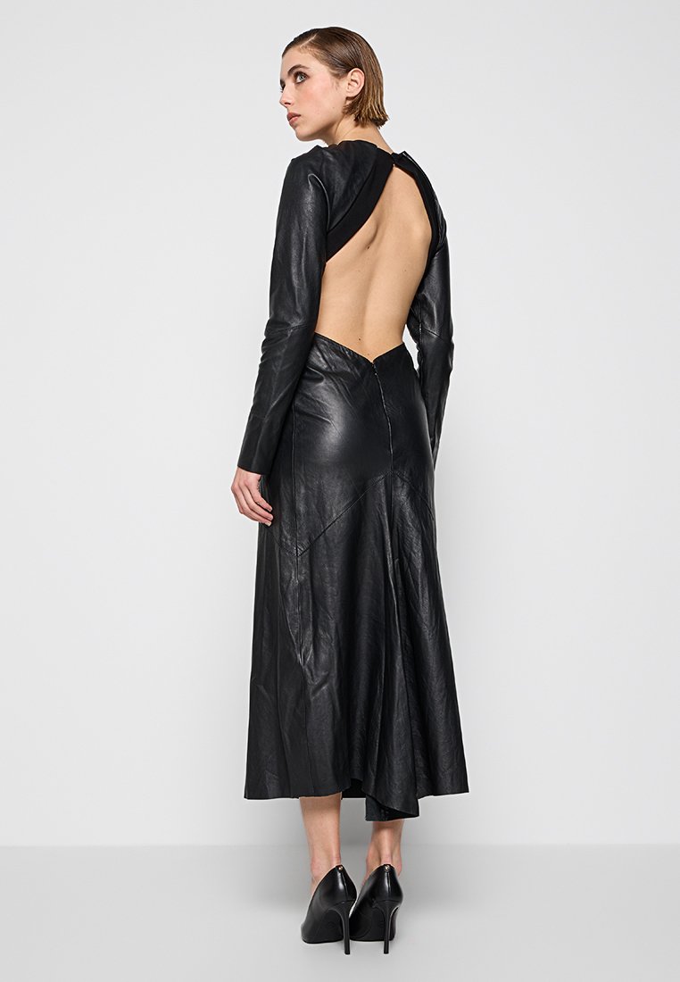 Czarna skórzana sukienka z odkrytym tyłem, z długimi rękawami, dopasowanym topem, rozkloszowanym dołem i widocznymi szwami. Uzupełniona czarnymi szpilkami.