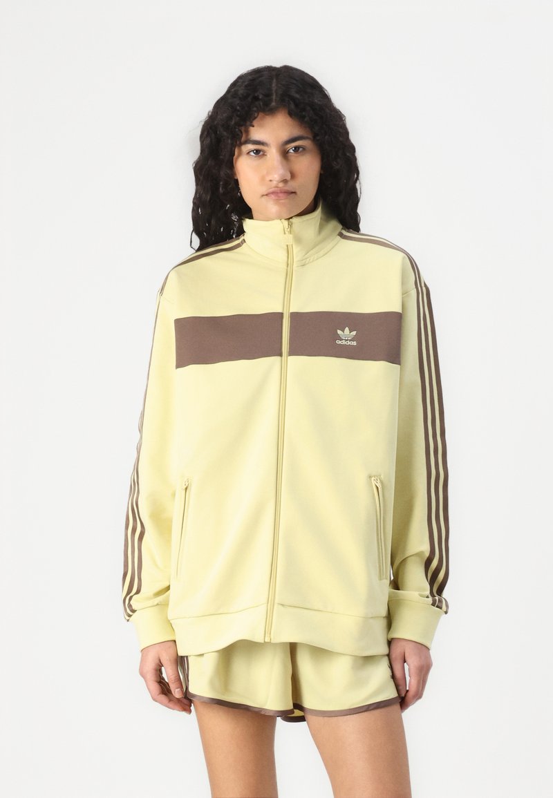 Yellow zip-up jacket with brown horizontal stripe, two side pockets, and three brown stripes running down each sleeve. Soft material.